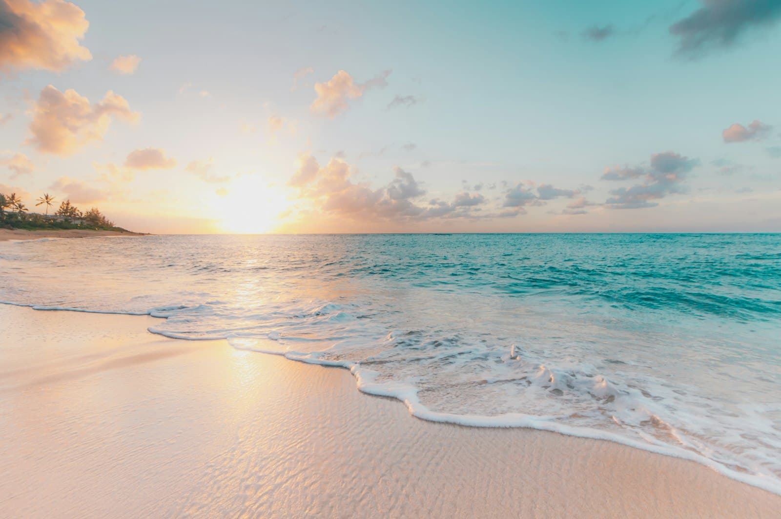 A beach in golden evening light with warm water and a soft sky