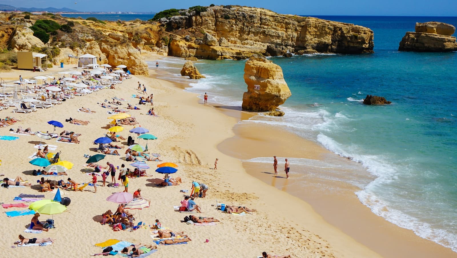 A sunny cove beach dotted with colorful umbrellas and swimmers